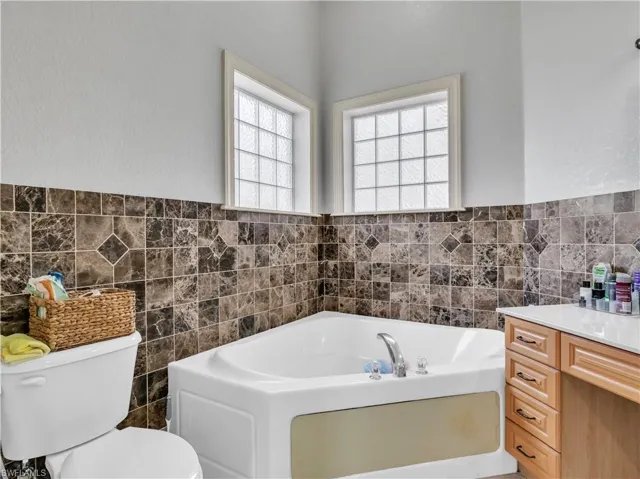 Bathroom with a washtub, toilet, tile walls, and vanity