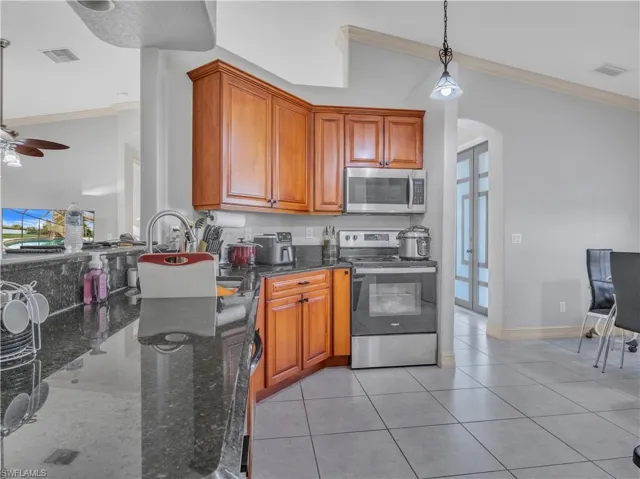 Kitchen featuring crown molding, pendant lighting, dark stone counters, and appliances with stainless steel finishes