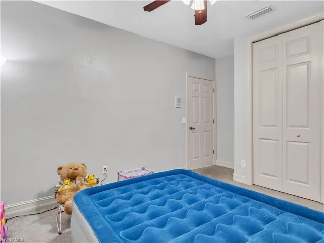 Carpeted bedroom with ceiling fan and a closet