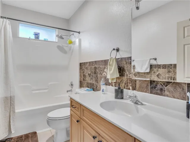 Full bathroom with shower / tub combo, tile patterned floors, vanity, tile walls, and toilet