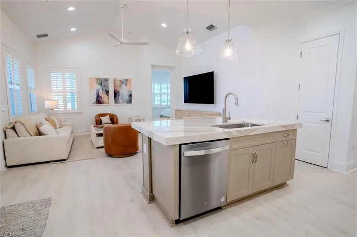 Kitchen with open floor plan, an island with sink, stainless steel dishwasher, light stone counters, and light wood-style floors