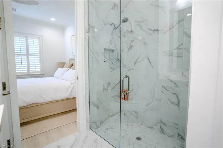 Ensuite bathroom featuring a marble finish shower, ornamental molding, recessed lighting, and marble look tile flooring