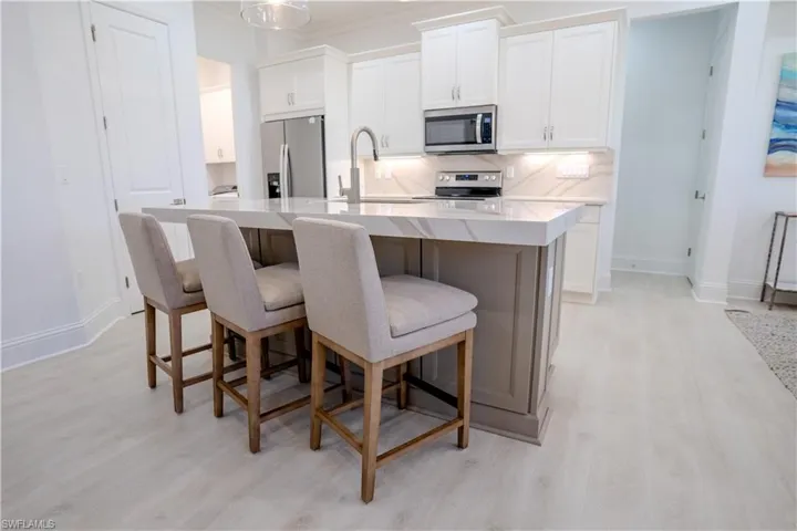 Kitchen with stainless steel appliances, a breakfast bar, white cabinets, light wood-style flooring, and an island with sink
