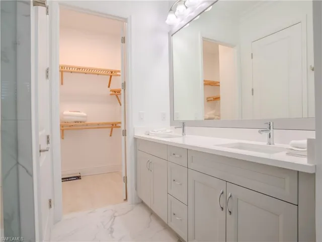 Bathroom with a spacious closet, double vanity, and light marble finish flooring