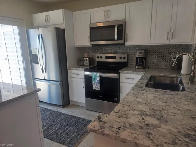 Kitchen with appliances with stainless steel finishes, white cabinets, light stone countertops, and decorative backsplash