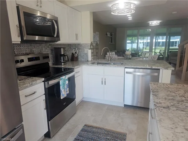 Kitchen featuring stainless steel appliances, backsplash, a peninsula, white cabinets, and light stone counters