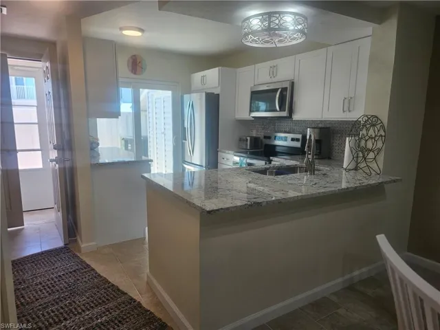 Kitchen with appliances with stainless steel finishes, light stone countertops, a peninsula, tasteful backsplash, and white cabinets
