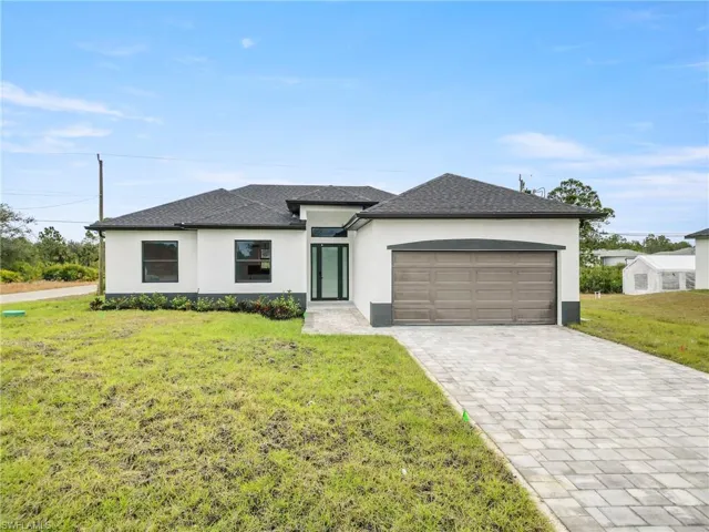Prairie-style home with an attached garage, decorative driveway, a front lawn, and stucco siding