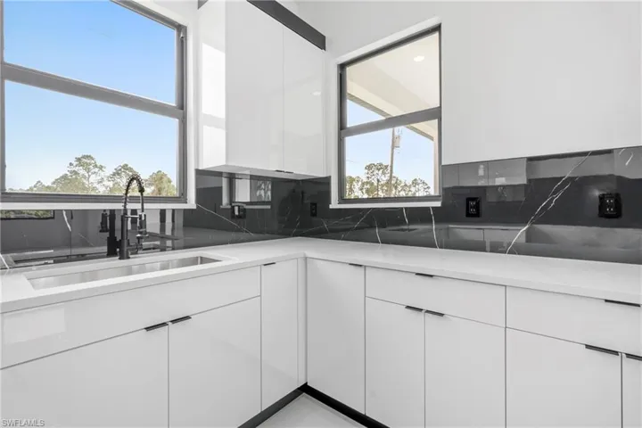 Kitchen featuring a sink, decorative backsplash, modern cabinets, and white cabinetry