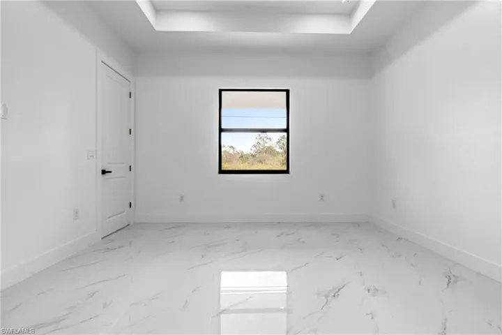 Empty room featuring baseboards, marble finish floor, and a raised ceiling
