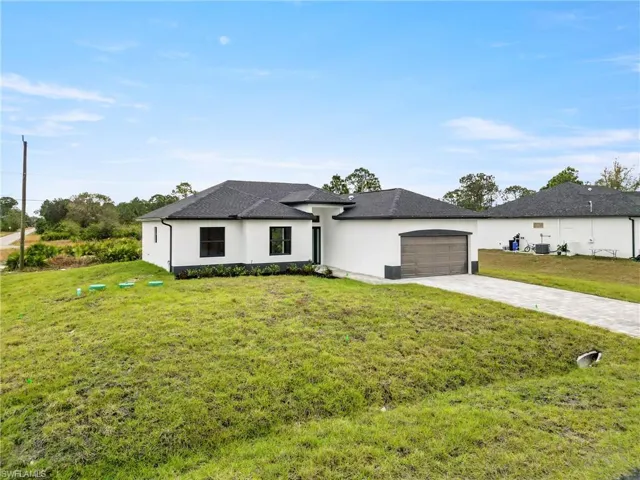 View of front of home with driveway, roof with shingles, a front yard, a garage, and stucco siding
