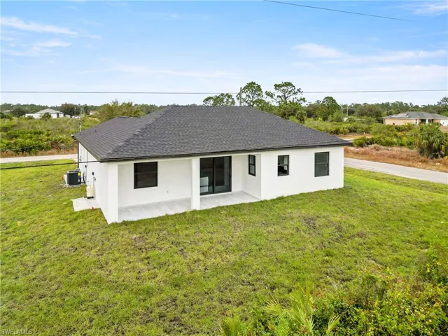 Back of property featuring roof with shingles, stucco siding, a patio area, central air condition unit, and a yard