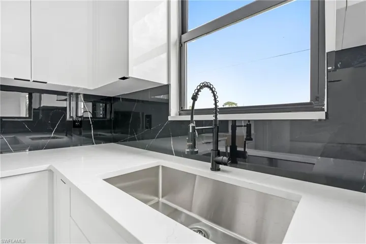 Details with a sink, light stone countertops, backsplash, and white cabinetry