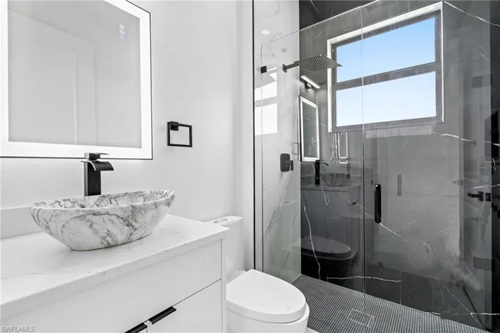 Full bath with a marble finish shower, vanity, and toilet
