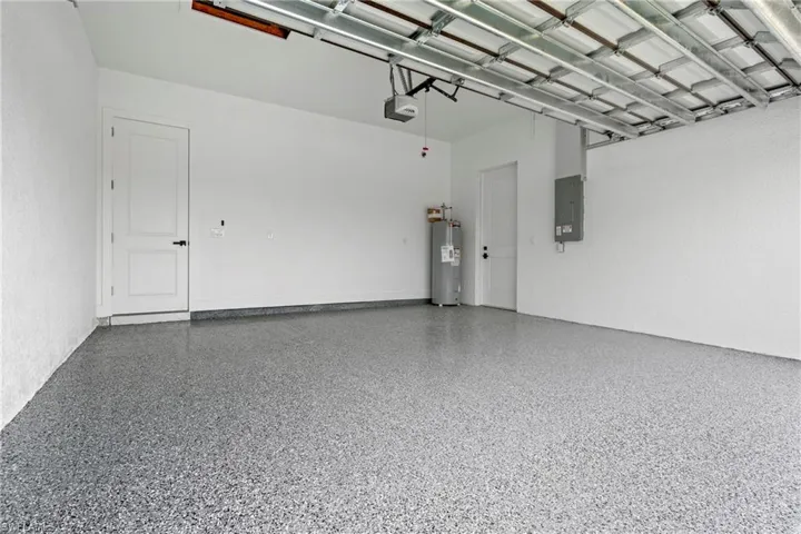 Garage with a garage door opener, electric panel, and electric water heater