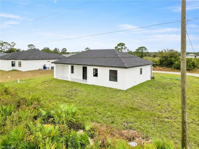 Rear view of property with a lawn, stucco siding, and roof with shingles