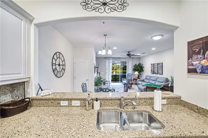 Kitchen featuring a ceiling fan, light stone counters, suspended lighting, arched walkways, and tasteful backsplash