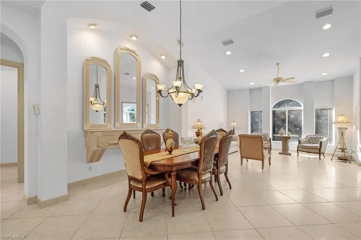 Dining space with vaulted ceiling, a wealth of natural light, ceiling fan with notable chandelier, and light tile patterned floors