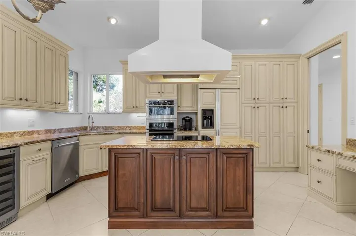 Kitchen with range hood, wine cooler, stainless steel appliances, light stone countertops, and cream cabinetry