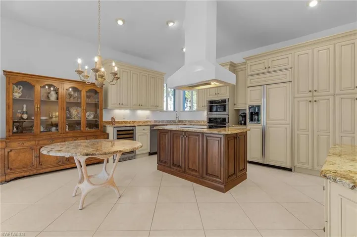 Kitchen with paneled built in refrigerator, cream cabinets, beverage cooler, and island exhaust hood