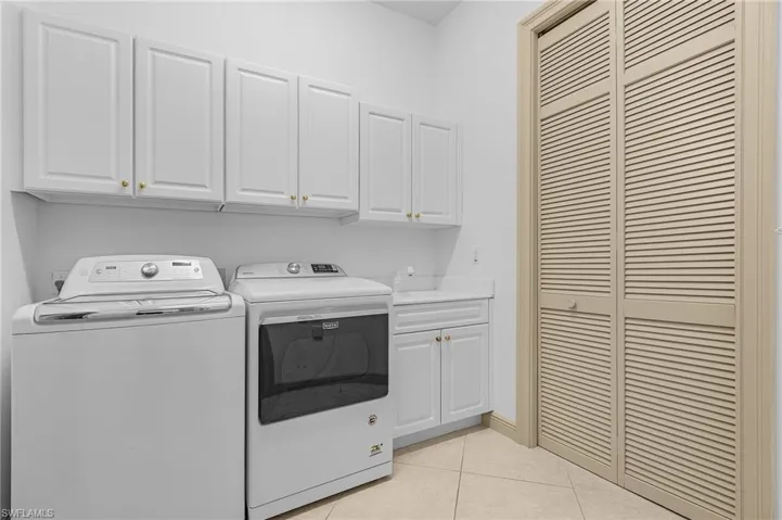 Laundry area featuring light tile patterned floors, cabinets, and washing machine and clothes dryer