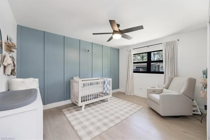 Bedroom with a nursery area, ceiling fan, and light wood-type flooring