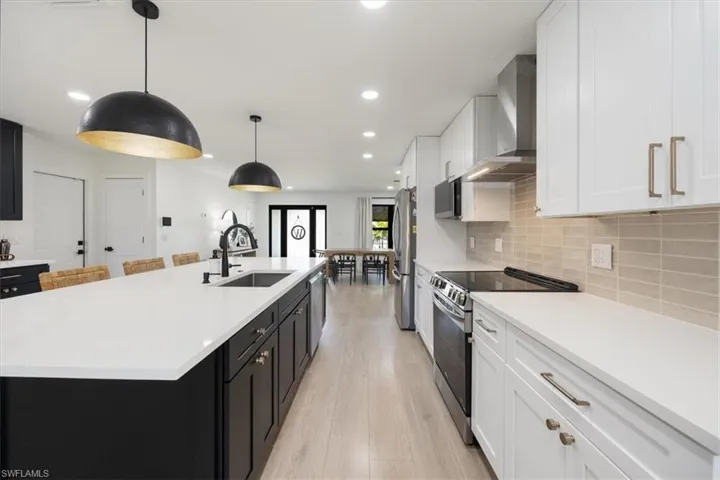 Kitchen featuring sink, stainless steel appliances, wall chimney exhaust hood, decorative light fixtures, and a large island with sink