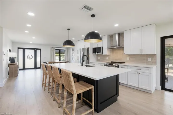Kitchen featuring appliances with stainless steel finishes, decorative light fixtures, white cabinets, wall chimney range hood, and a center island with sink