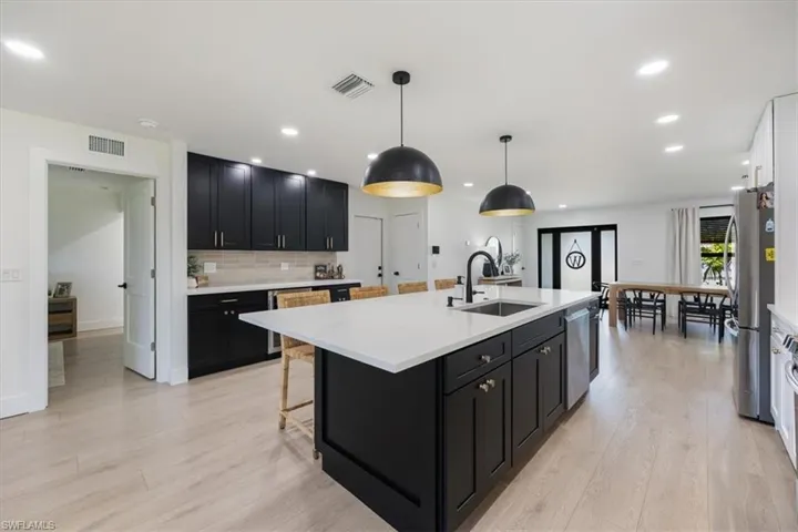 Kitchen with sink, appliances with stainless steel finishes, hanging light fixtures, an island with sink, and decorative backsplash