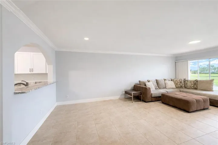 Living area with ornamental molding, light tile patterned floors, recessed lighting, and arched walkways