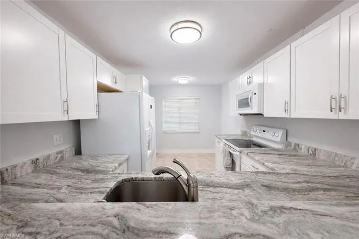 Kitchen featuring white cabinetry, white appliances, and light stone counters
