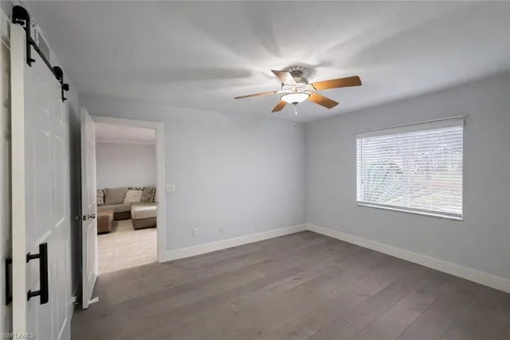 Unfurnished bedroom featuring a barn door, light wood-style floors, and ceiling fan