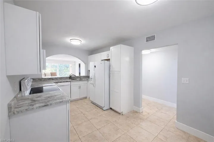 Kitchen featuring white appliances, white cabinets, arched walkways, and light stone counters