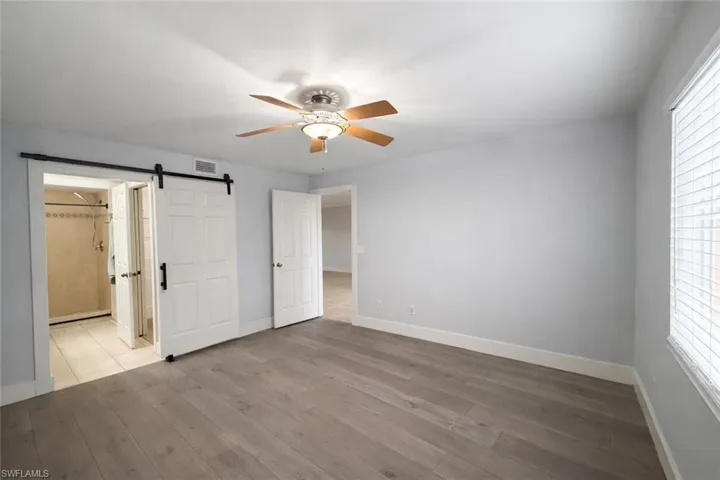 Unfurnished bedroom featuring a barn door, hardwood / wood-style floors, a ceiling fan, and multiple windows