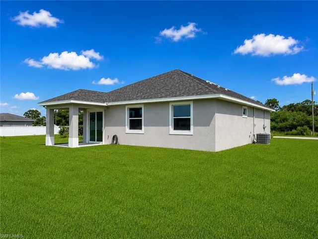Expansive green lawn with a covered patio, multiple windows, and a sliding glass door