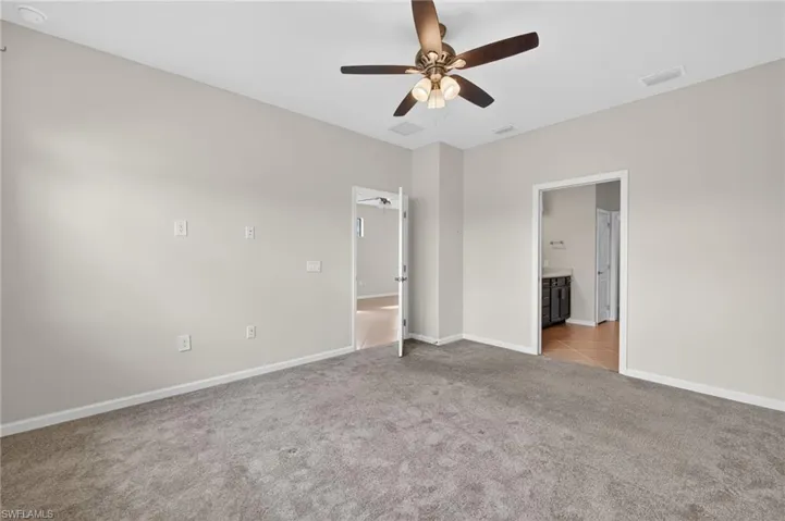 Primary Bedroom with light colored carpet, connected bathroom, and a ceiling fan