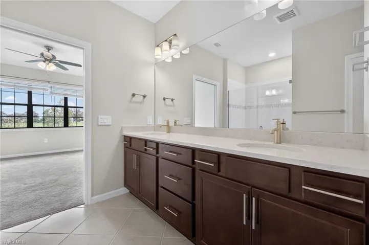 Primary Bathroom with light colored carpet, a shower stall, double vanity, light tile patterned floors, and ceiling fan