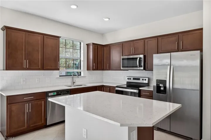 Kitchen with stainless steel appliances, light stone countertops, backsplash, light tile patterned floors, and a center island