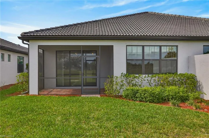 Rear view of property with a sunroom, a tile roof, a lawn, and stucco siding