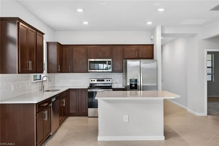 Kitchen with stainless steel appliances, dark wood finish cabinetry, light tile patterned floors, a center island, and recessed lighting