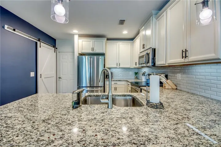 Kitchen with decorative backsplash, appliances with stainless steel finishes, white cabinets, and a barn door