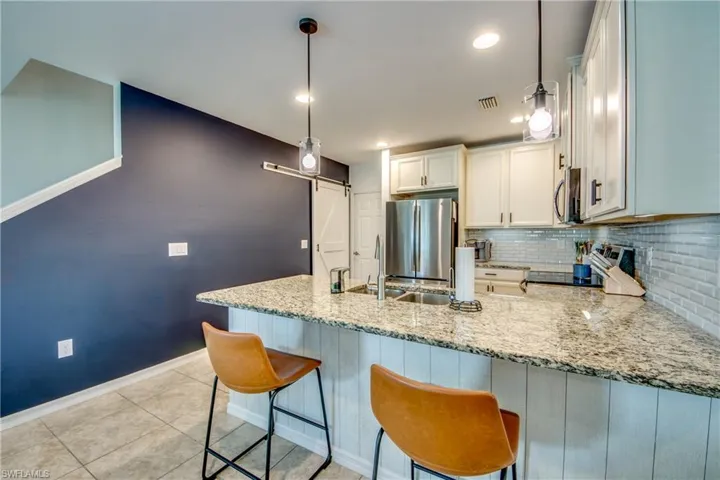 Kitchen featuring decorative backsplash, pendant lighting, stainless steel appliances, and white cabinets