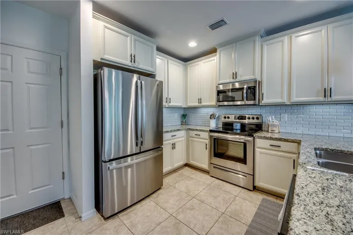 Kitchen featuring decorative backsplash, light tile patterned floors, light stone counters, and stainless steel appliances