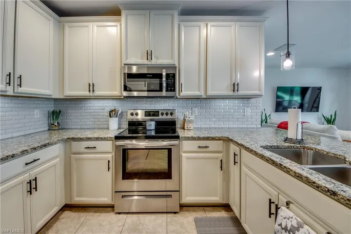 Kitchen featuring appliances with stainless steel finishes, hanging light fixtures, light tile patterned floors, decorative backsplash, and light stone countertops