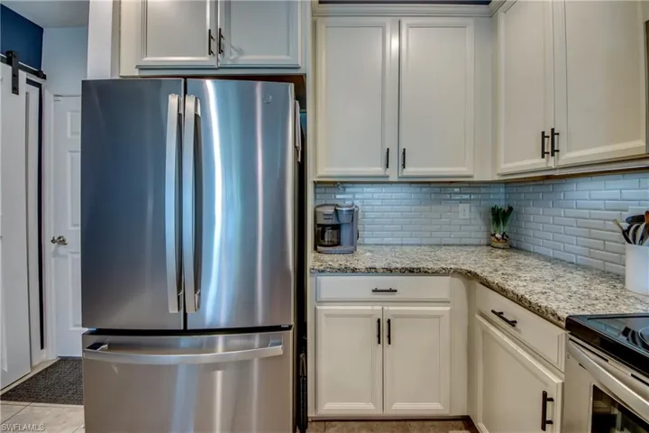 Kitchen featuring light tile patterned flooring, stainless steel fridge, light stone countertops, and white cabinets