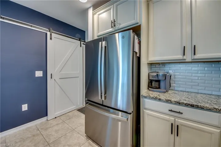 Kitchen featuring light stone counters, stainless steel refrigerator, a barn door, backsplash, and light tile patterned flooring