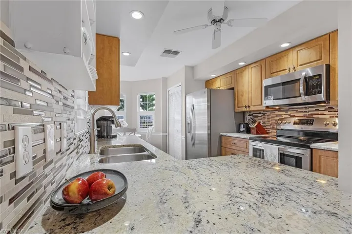 Kitchen featuring sink, decorative backsplash, ceiling fan, light stone counters, and stainless steel appliances