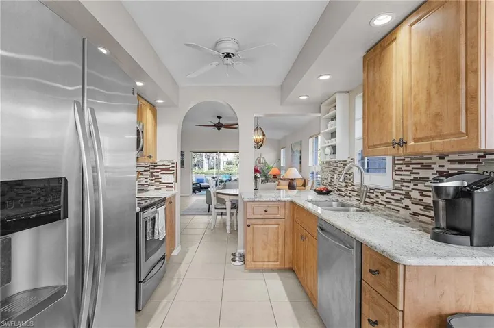 Kitchen with sink, light tile patterned floors, light stone counters, kitchen peninsula, and stainless steel appliances