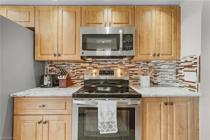 Kitchen featuring light stone countertops, appliances with stainless steel finishes, backsplash, and light brown cabinetry