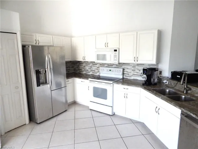 Kitchen with light tile patterned floors, backsplash, stainless steel appliances, sink, and white cabinets
